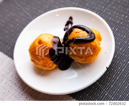 Sweet baked profiteroles with hot chocolate cream at plate Sweet baked profiteroles with hot chocolate cream at plate 72802632
