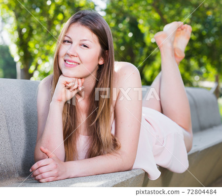 Cheerful young female is lying on bench in her free time 72804484