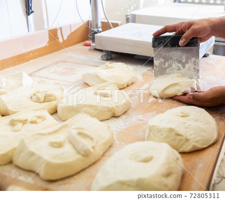Hands of baker portioning raw dough with scraper 72805311
