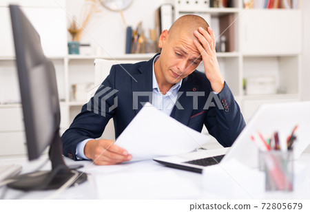 Upset man working with laptop and papers Upset man working with laptop and papers 72805679