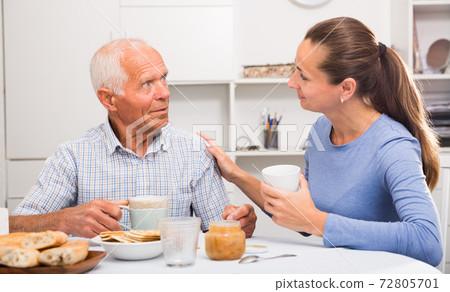 Mature man with daughter talking at table with cup of tea Mature man with daughter talking at table with cup of tea 72805701