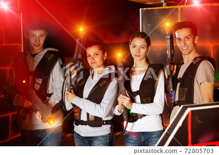 Happy young people with laser pistols posing together in bright beams in laser tag labyrinth Happy young people with laser pistols posing together in bright beams in laser tag labyrinth 72805703