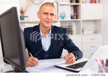 Positive businessman working with laptop and documents Positive businessman working with laptop and documents 72805766