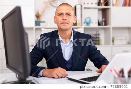 Positive businessman working with laptop and documents Positive businessman working with laptop and documents 72805901
