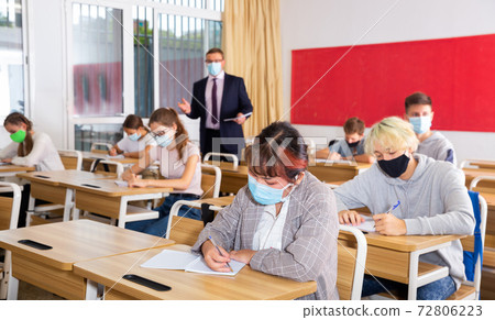 Teacher in protective mask explains to the students the subject of instruction in classroom 72806223