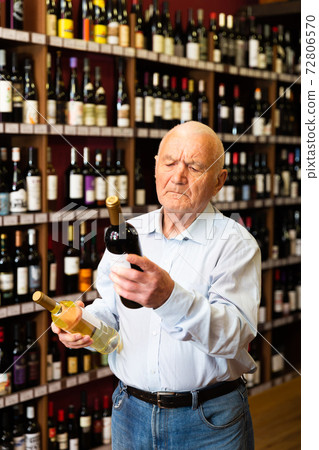 Serious retiree chooses white and red wine in a liquor store Serious retiree chooses white and red wine in a liquor store 72806570