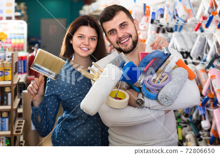 Young cheerful couple demonstrating tools for house renovating in paint store 72806650
