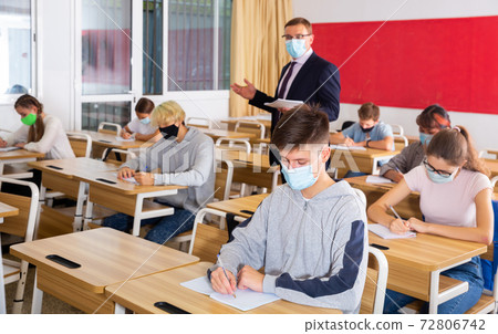 Teenagers in protective masks studying in classroom with teacher Teenagers in protective masks studying in classroom with teacher 72806742
