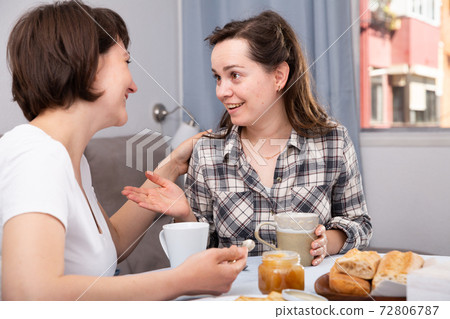 Two woman friends talking and drinking tea in the kitchen Two woman friends talking and drinking tea in the kitchen 72806787