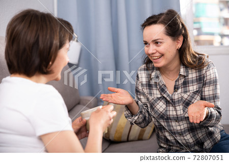 Smiling young female friends gossiping on sofa in home interior Smiling young female friends gossiping on sofa in home interior 72807051