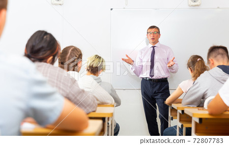 Male teacher lecturing to students at classroom Male teacher lecturing to students at classroom 72807783
