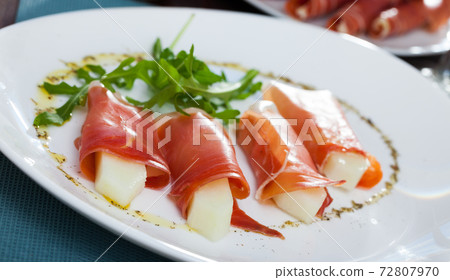 Rolls of iberian jamon stuffed with melon at plate with arugula 72807970