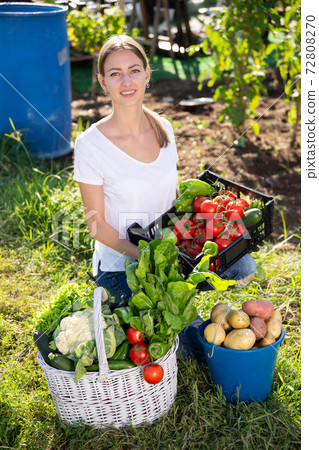 Young woman gardener holding basket with harvest of vegetables Young woman gardener holding basket with harvest of vegetables 72808270