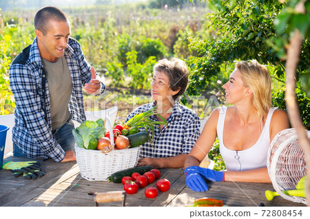 Family in garden talking after harvesting vegetables 72808454