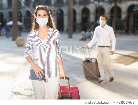 Female traveler in medical mask strolling with luggage along city Female traveler in medical mask strolling with luggage along city 72808462
