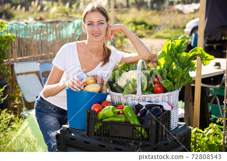 Young woman gardener with harvest of vegetables and greens 72808543