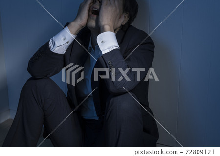 一位商人坐在黑暗的房間裡的地板上 一位商人坐在黑暗的房間裡的地板上 72809121