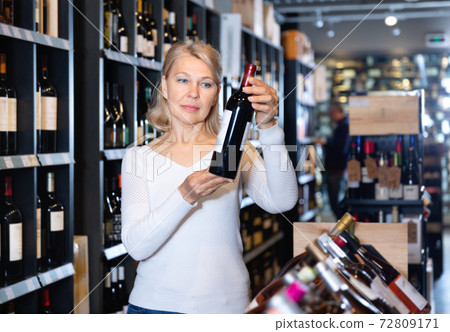 Portrait of mature woman visiting winehouse in search of bottle of good wine 72809171