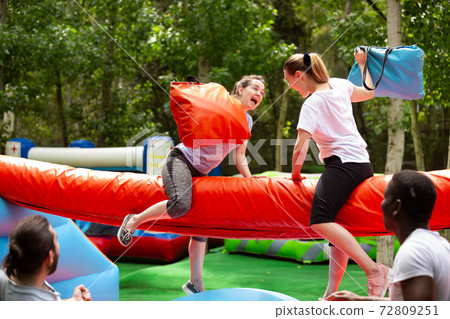 Women fighting by pillows on inflatable beam 72809251