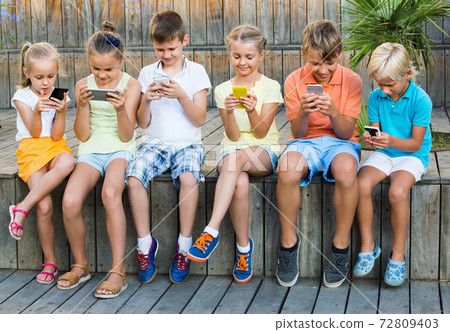 Busy children holding smartphones and sitting Busy children holding smartphones and sitting 72809403