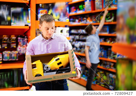 Portrait of positive adult man buying toy cement mixer machine in modern toy store 72809427