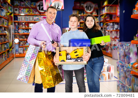 Portrait of friendly family with teenage son holding new toys purchased in kids mall Portrait of friendly family with teenage son holding new toys purchased in kids mall 72809481