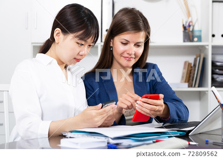 Two women write sms by phone in the office 72809562