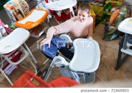 Woman buyer choosing chair for eating in the shop for children Woman buyer choosing chair for eating in the shop for children 72809803