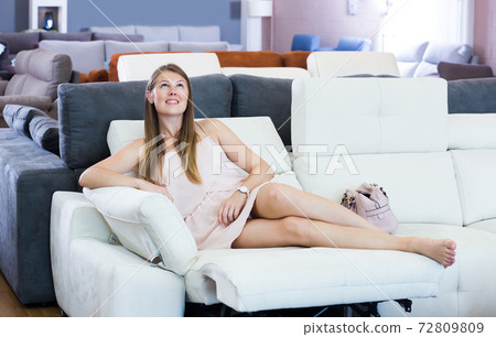 Happy woman lying barefoot on sofa with pillow 72809809
