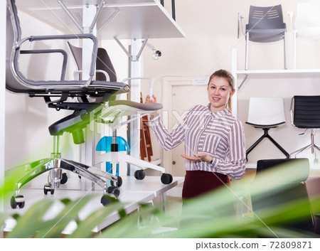 Salesgirl in furniture salon suggesting swivel chair 72809871
