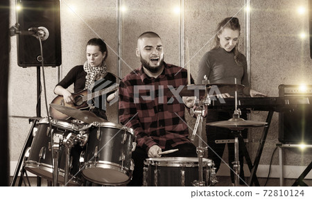 Expressive drummer with his bandmates practicing in rehearsal ro Expressive drummer with his bandmates practicing in rehearsal ro 72810124