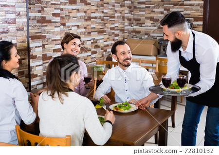 Male waiter carrying order for visitors in country restaurant 72810132
