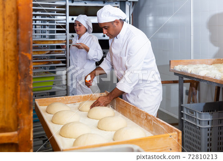 Baker sprinkling water on raw formed bread before baking Baker sprinkling water on raw formed bread before baking 72810213