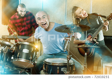 Expressive drummer with his bandmates practicing in rehearsal ro Expressive drummer with his bandmates practicing in rehearsal ro 72810231