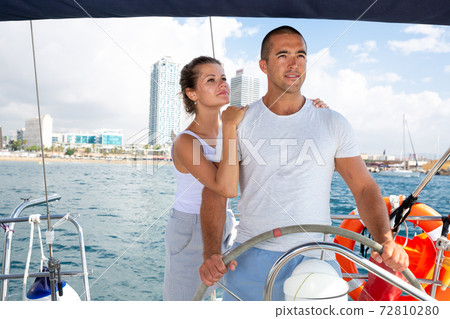 Woman and man steering yacht along shoreline of Spain 72810280