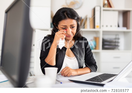Frustrated female sitting in office with papers and laptop Frustrated female sitting in office with papers and laptop 72810377