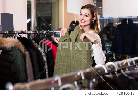 woman choosing green quilted jacket in women’s cloths store woman choosing green quilted jacket in women’s cloths store 72810515