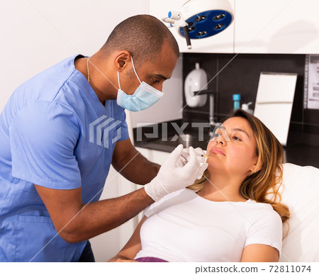 Male beautician performing face contouring injections to female Male beautician performing face contouring injections to female 72811074