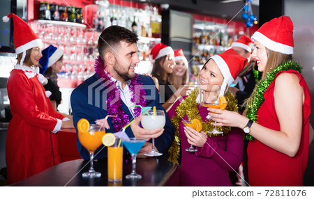Man and two women with cocktails in Santa hats celebrating at nightclub 72811076