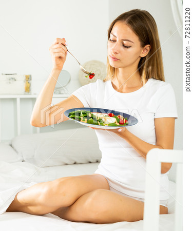 Cheerful young girl in lingerie having a salad while laying in the bed Cheerful young girl in lingerie having a salad while laying in the bed 72811220