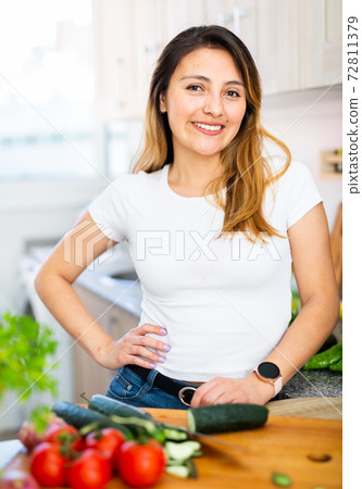 Woman is standing near table and cutting vegetables in the kitchen at the home Woman is standing near table and cutting vegetables in the kitchen at the home 72811379