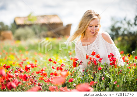 Beautiful young female in white dress in poppy field of wild flowers Beautiful young female in white dress in poppy field of wild flowers 72811770