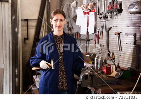 Portrait of young smiling woman in uniform who with a hammer in her hand Portrait of young smiling woman in uniform who with a hammer in her hand 72811835