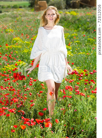 Woman wearing white dress walking through a poppy field and enjoying Woman wearing white dress walking through a poppy field and enjoying 72812016