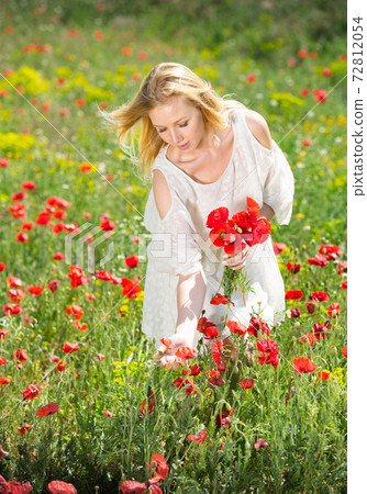 Beautiful young female in white dress holding bouquet of poppy flowers 72812054