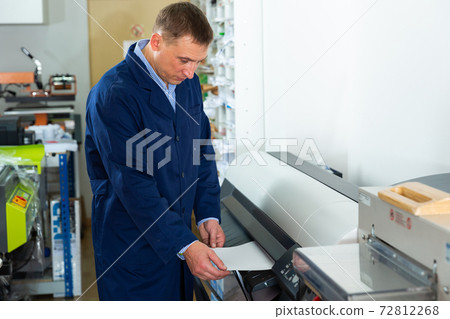 Service man uses plotter in printing shop 72812268