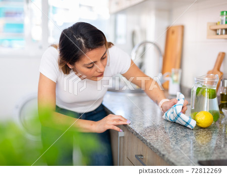 Young latino woman cleans the kitchen table 72812269
