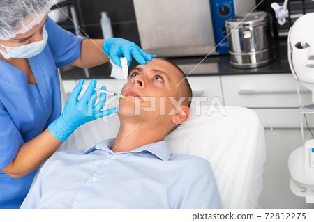 Man receiving facial contouring injections in cosmetology clinic Man receiving facial contouring injections in cosmetology clinic 72812275