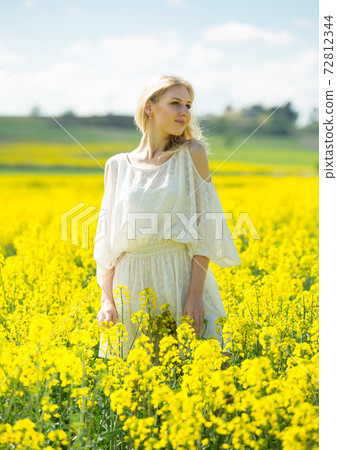 Young woman in yellow oilseed rape field posing in white dress Young woman in yellow oilseed rape field posing in white dress 72812344