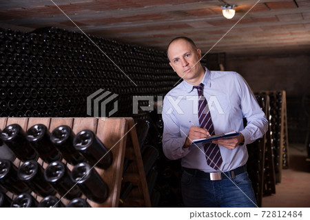 Wine producer with clipboard in wine cellar 72812484